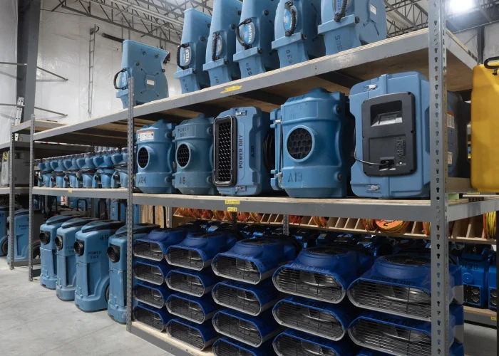 Rows of industrial air movers and dehumidifiers staged on warehouse shelving — water and fire restoration leads in Kansas